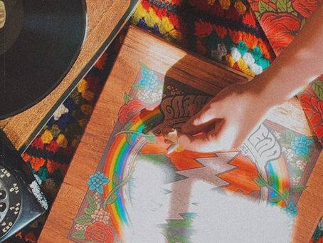 Overhead view of hands passing rolled cigarette over crocheted blanket, album covers, and vinyl record