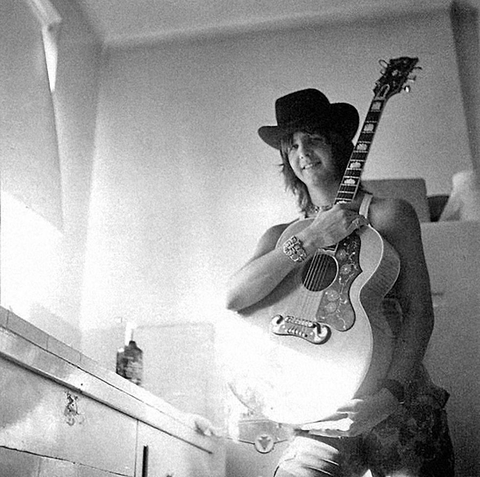 Black and white photo of long-haired man in cowboy hat holding acoustic. guitar