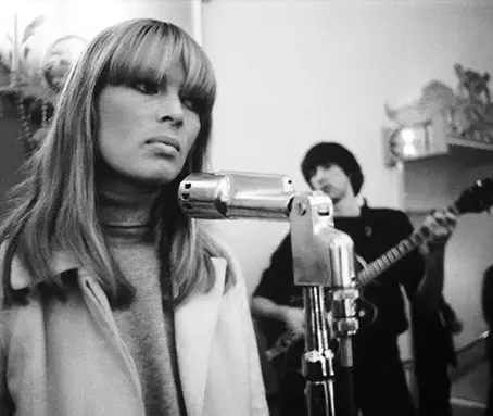 Black and white photo of blonde woman in white jacket in front of microphone