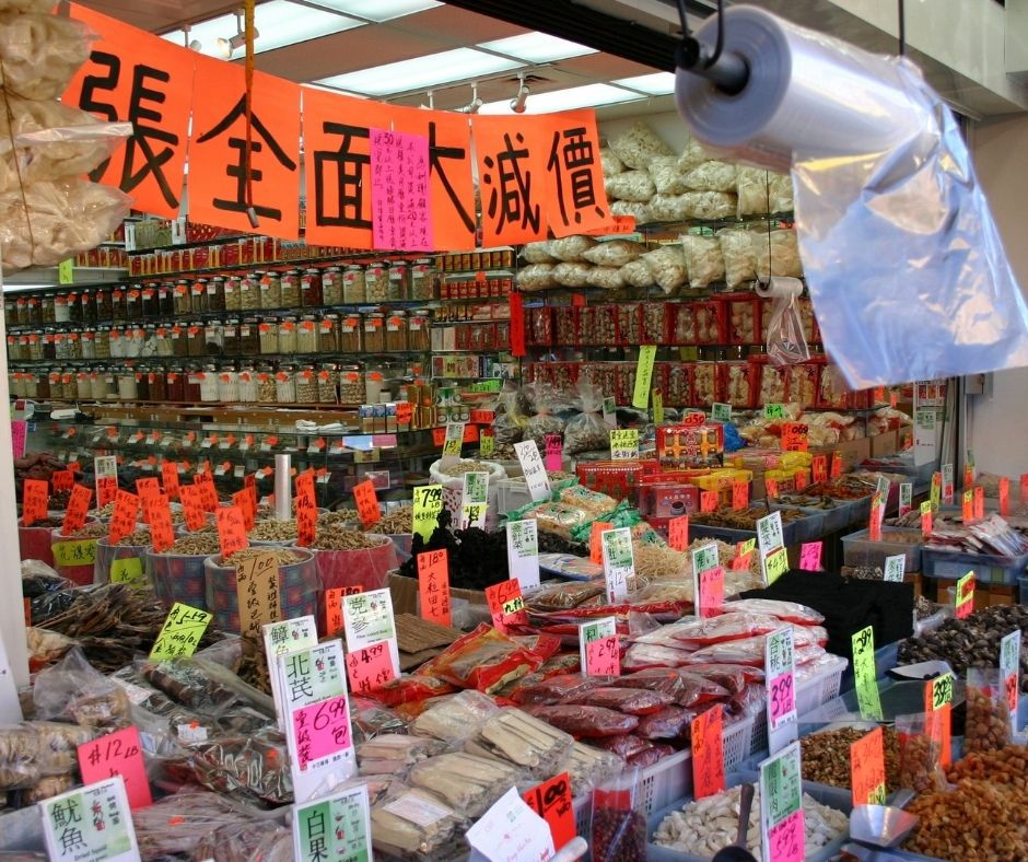 Tabletop display of items with signage in both Chinese and English line the front of the photo. Glass jars and bags of products line the wall.