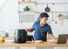 homem-usa-fritadeira-eletrica-air-fryer-e-mexe-no-notebook-laptop-na-cozinha-1642017839988
