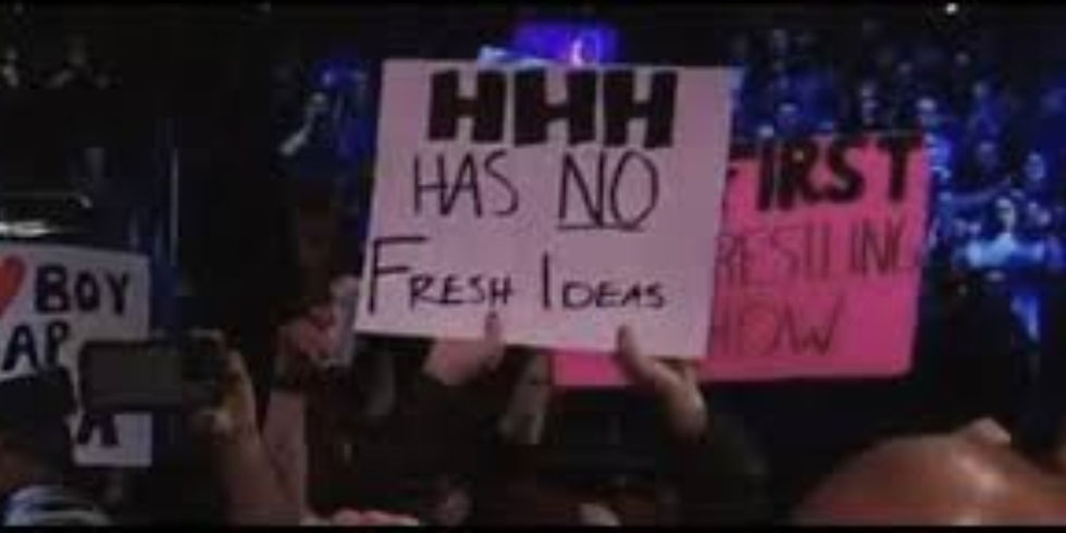 frustrated wwe fan holding a sign at an event saying "Triple H has no fresh ideas"
