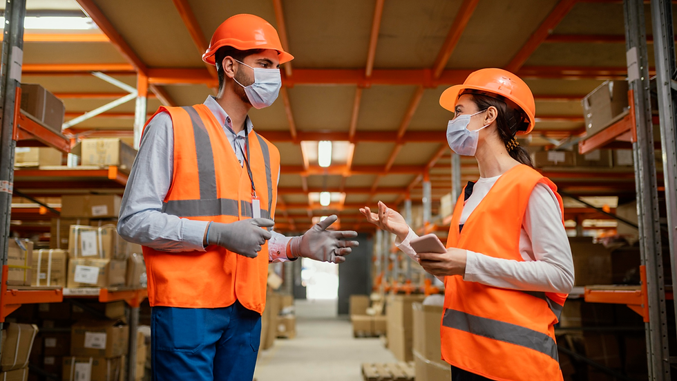 Two warehouse workers wearing PPE discussing workplace safety in a logistics environment during operational activity.