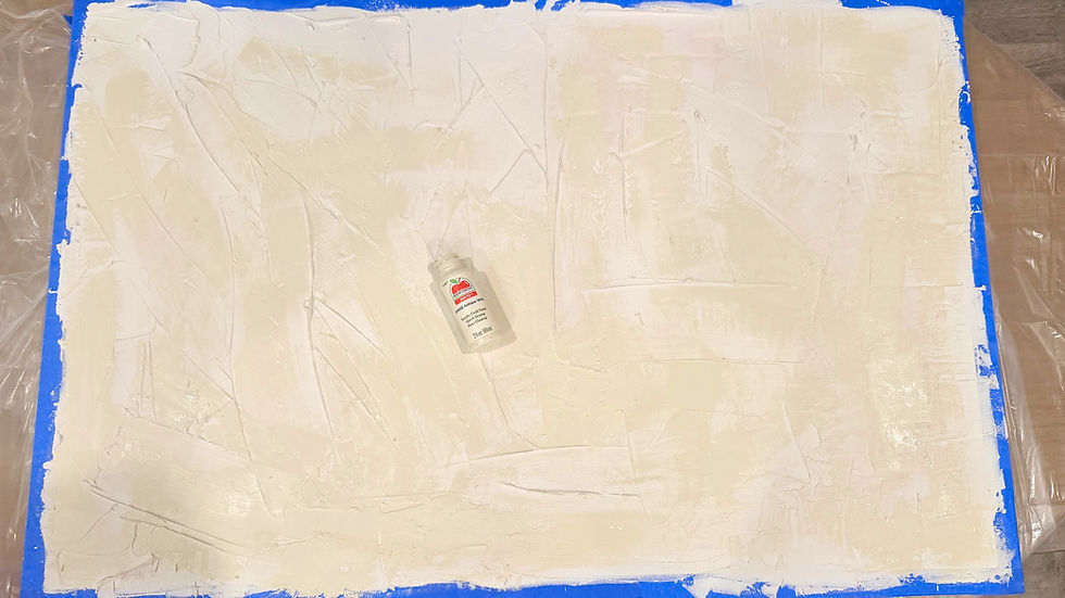 A textured canvas is covered with a soft layer of antique white paint, exhibiting subtle variations and depth. A bottle of paint rests on the canvas, surrounded by painter's tape, suggesting an ongoing creative process.