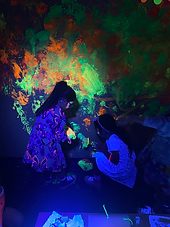 Kids exploring neon paint in the Glow in the Dark Splatter Room at an art birthday party.