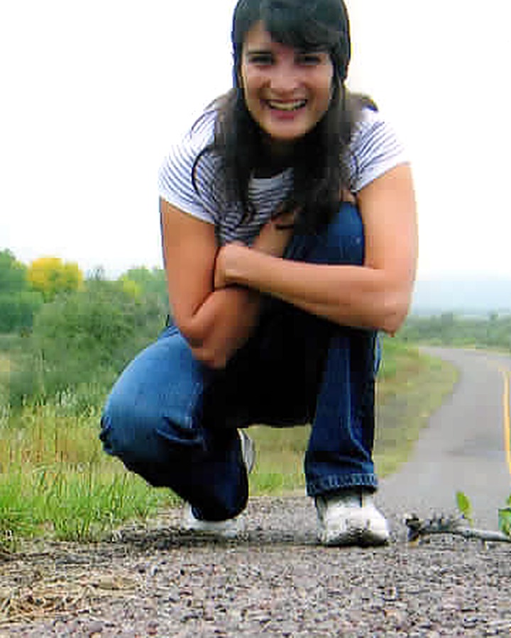 Dr. Nilou Zahedi, smiling, crouched on a country road