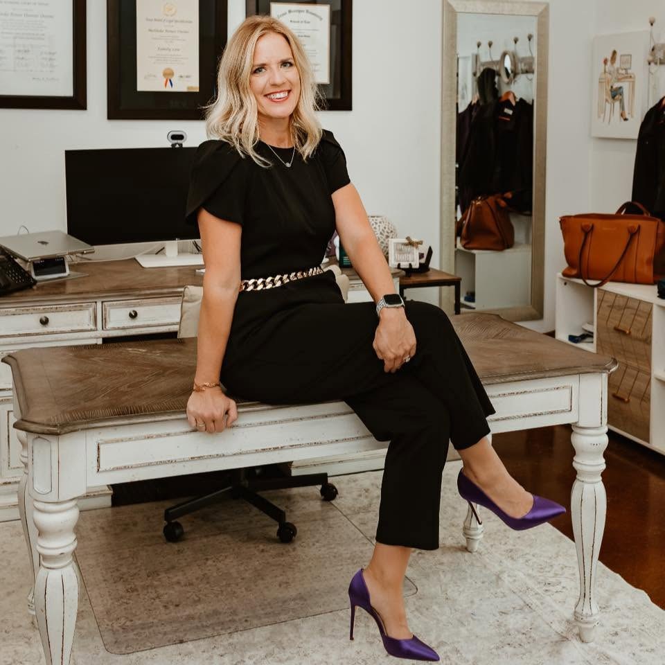 Melinda Owens, attorney and founder, seated on the desk in her Granbury law office