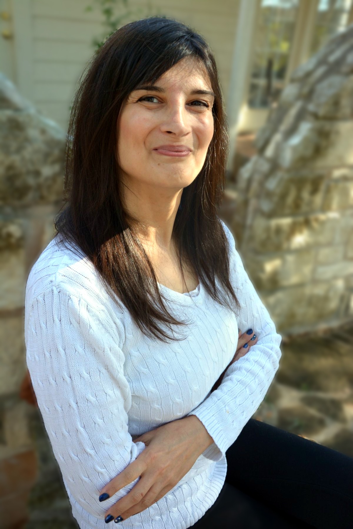 Dr. Nilou Zahedi, smiling, seated outdoors by a stone wall