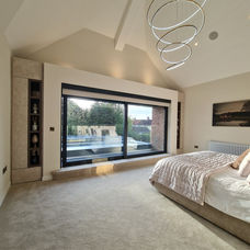 Bespoke display cabinets custom-made on window sides in a luxury bedroom by KV Designs Leeds, featuring tall light-toned alcove storage units with open shelving flanking a large panoramic sliding window under a vaulted ceiling.