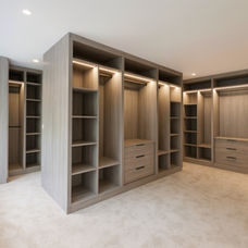 Luxury custom walk-in wardrobe by KV Designs Leeds, showcasing a modern light grey wood grain finish, open hanging rails, custom drawer units, and built-in warm LED vertical strip lighting.