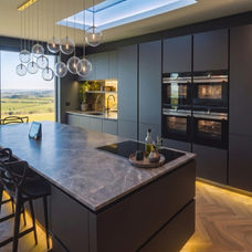 Modern bespoke dark gray kitchen by KV Designs Leeds, featuring a large marble-veined island, integrated double ovens, and warm under-island LED lighting.