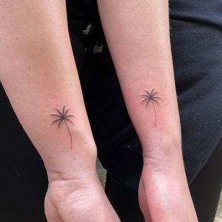 Two people showing matching minimalist fine line palm tree tattoos on their wrists, created at a professional tattoo studio in Budva