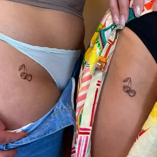 Fine line cherry tattoo on the upper thigh by a tattoo artist in Budva, Montenegro. featuring minimalist black and grey shading.