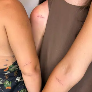 Three friends showing their matching minimalist fine line tattoos on arms and shoulder, done at a professional Budva tattoo studio.