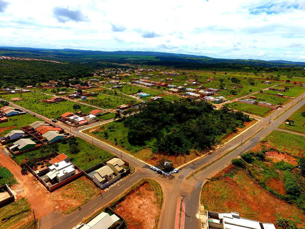 Vista aérea de bairro residencial com ruas em cruz, casas baixas e áreas verdes, sob céu nublado.