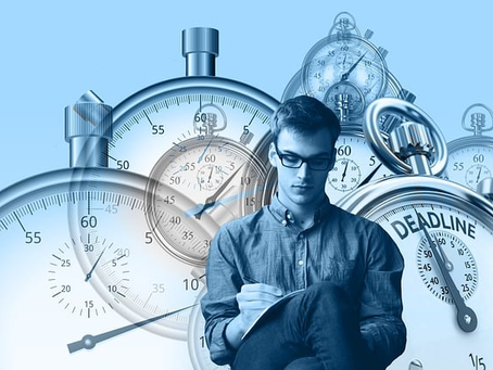 Seated male adult with pen and pad in his lap and surrounded by stopwatches of various sizes and styles in the background.