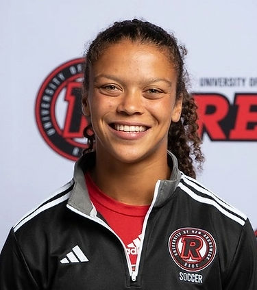 Close-up of a woman with long, curly hair in a ponytail, wearing a black, red, white, and grey shirt