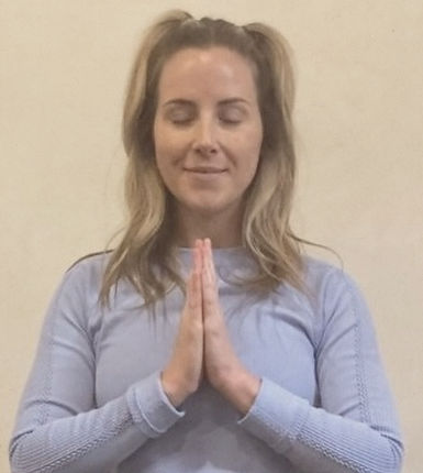 Close-up of a woman with long blonde hair, wearing a light blue shirt, and with hands in prayer position