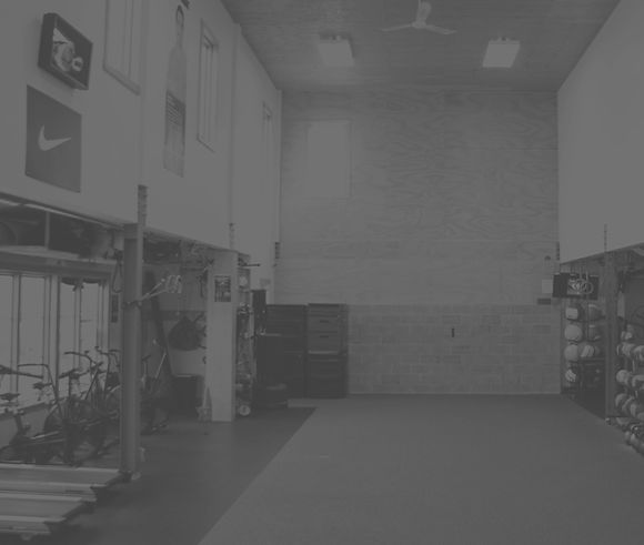 Black and white image of a high-ceilinged room, with treadmills, stationary bikes, and weights off to the sides
