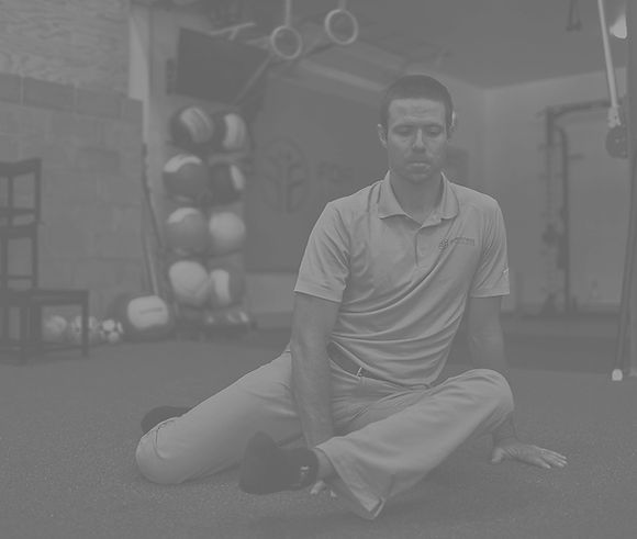Black and white image of a man, with his eyes closed, posed in a seated stretch