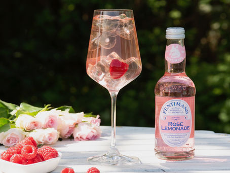 Stemmed glass full of pink liquid next to bottle of rose lemonade