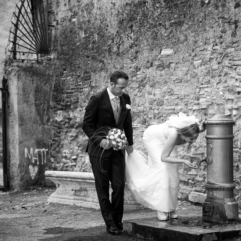 una bellissima fotografia in bianco e nero che ritrae gli sposi mentre si rinfrescano ad una fontanella tipica romana "nasone".