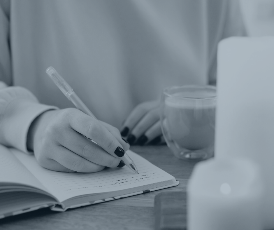 A woman journals on her English progress this year with some lit candles and a cup of coffee