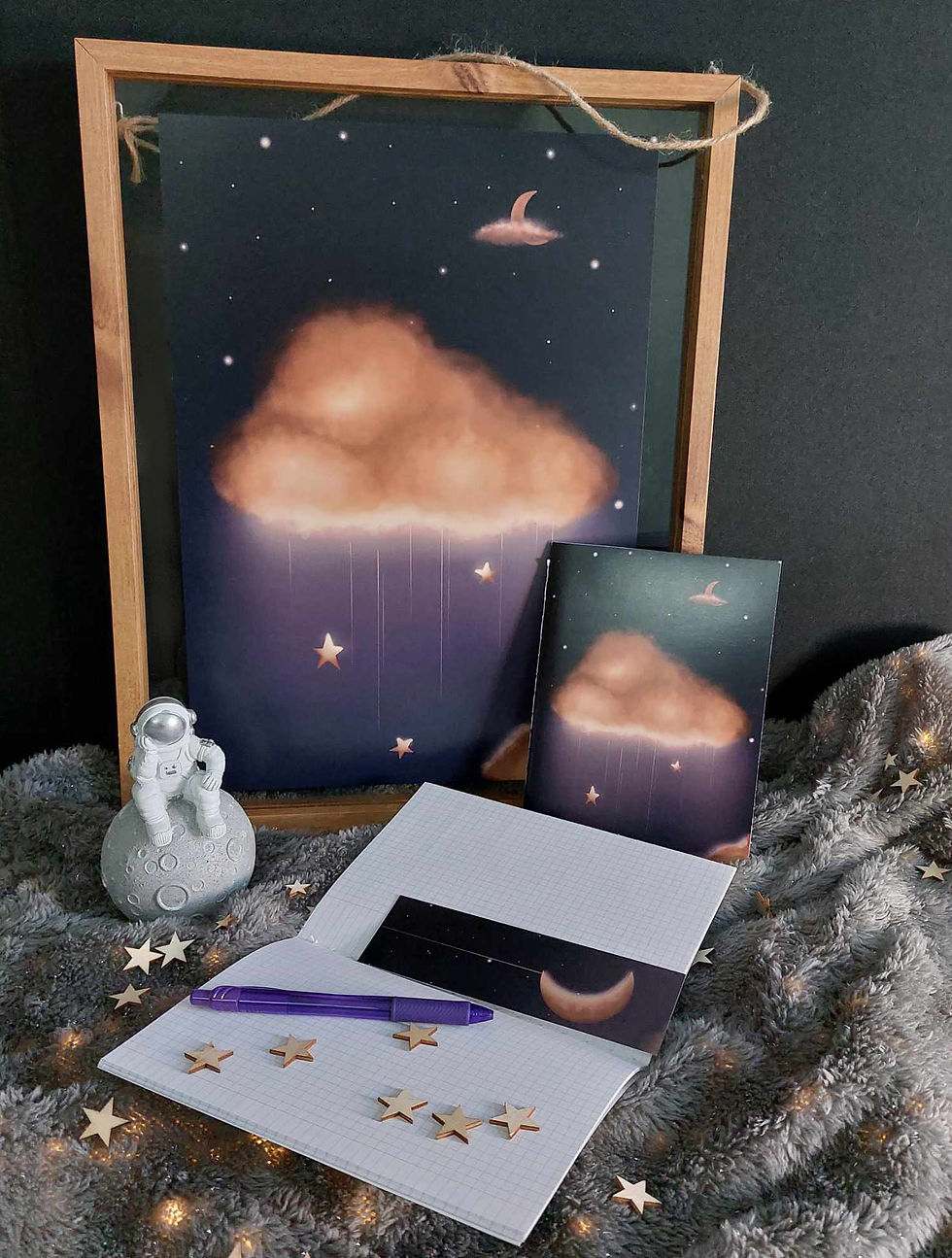 Sur décor étoilé, un pack montrant une illustration dans un cadre, 2 carnets dont un ouvert avec un marque page dessus