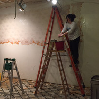 Two women removing old wallpaper from walls during renovation.