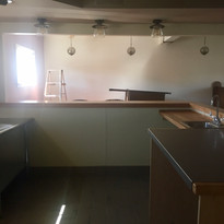 Commercial kitchen with shiny steel table, wooden counters, sink, and ladder.