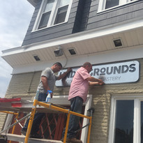 Men installing "GROUNDS ROASTERY" sign onto a building exterior.