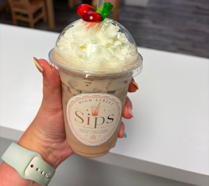 Hand holding an iced coffee-style drink with whipped cream