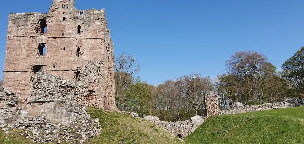 Stone castle ruins under clear blue sky, surrounded by green grass and trees. The scene evokes a sense of history and tranquility.