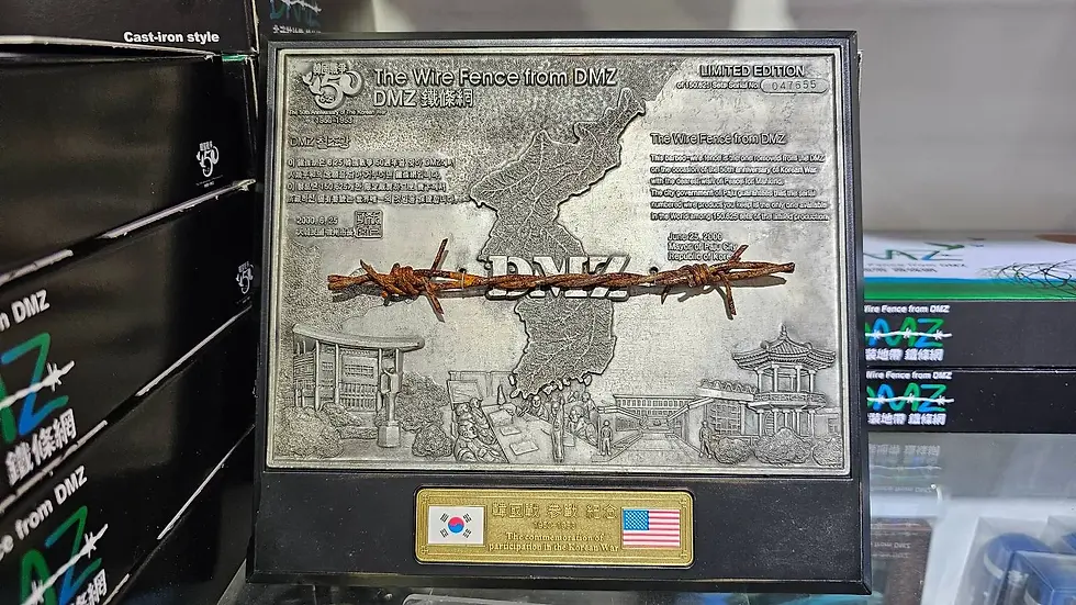 Metal plaque featuring a barbed wire from DMZ, map engraving, Korean and U.S. flags, and text about Korean War commemorations. Boxes in background.