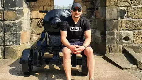 Leon seated beside a historic cannon at Edinburgh Castle with stone walls and city views.