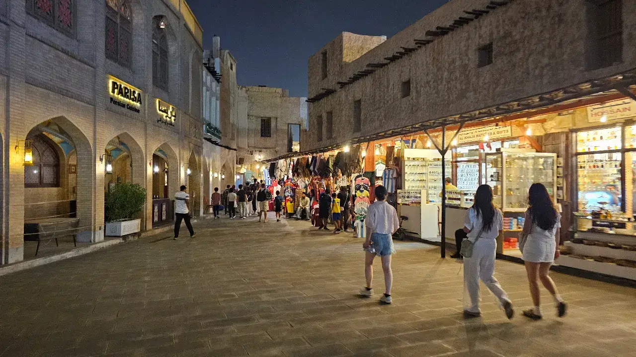People strolling along the vibrant outdoor square at Souq Waqif in Doha, Qatar, under evening string lights.