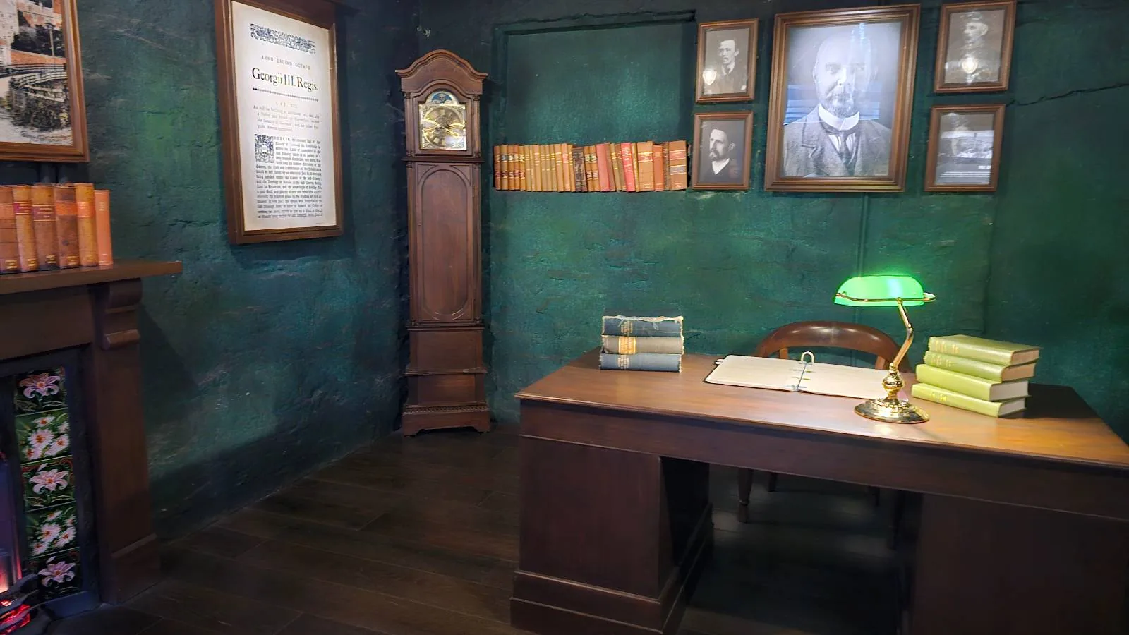 Vintage office interior with a wooden desk, lamp, books, and framed pictures on dark green walls, featuring a grandfather clock.