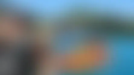 Smiling man and woman with hat by Lake Ohrid. Background: blue water, boat, green hills, houses. Text: Lake Ohrid. Sunny, vibrant scene.