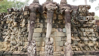 Ancient stone wall with detailed carvings depicting three elephants among various figures at the Terrace of the Elephants in Angkor Thom, Cambodia.