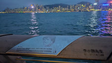 A waterfront plaque dedicated to Bruce Lee with a city skyline and mountains illuminated at dusk in the background.
