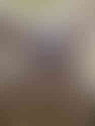 View looking up through a narrow, stone-lined shaft or tunnel with rough, stacked rocks, leading to a small opening at the top where daylight is visible.