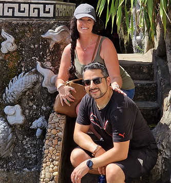 A woman and man pose together on stone steps beside an ornate monument with Asian script and dragon sculptures, set among the lush greenery and limestone peaks of Da Nangโs Marble Mountains on a sunny day.