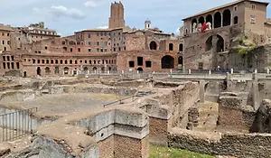 The historic archaeological ruins of Trajan’s Forum in Rome featuring ancient stone walls and brick structures under a blue sky.