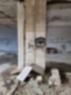 An abandoned interior with graffiti, including a drawn eye on a pillar, and debris on the floor.