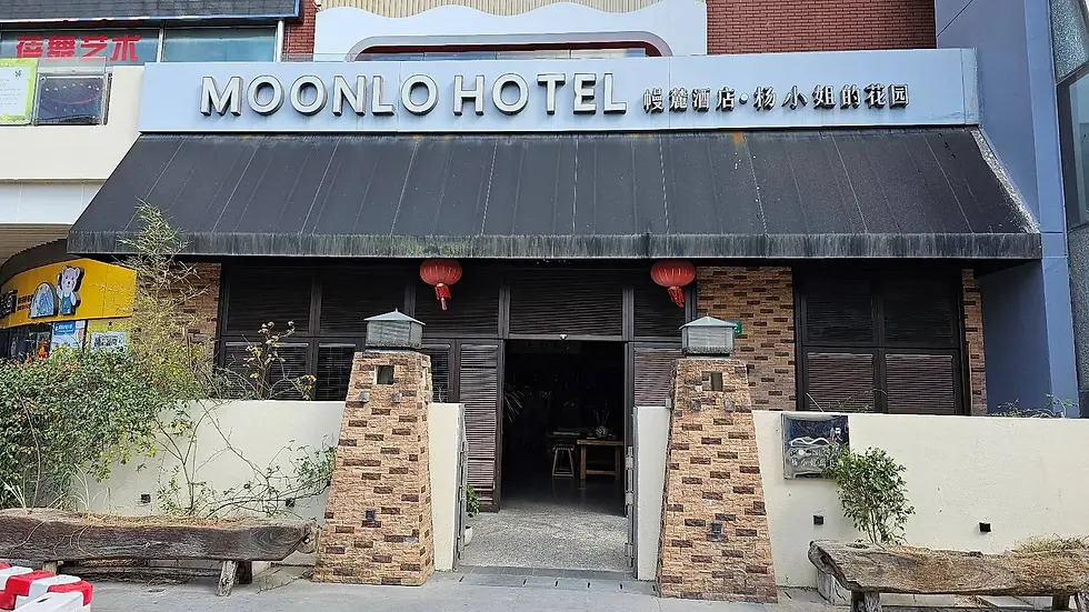 Facade of Moonlo Hotel with black awning, brick pillars, red lanterns, and plants. Visible signs in English and Chinese characters.