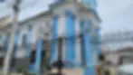 Blue and white church under renovation, surrounded by black wrought iron fence. Scaffolding set up, lamp posts and a clear sky in the background.