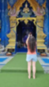 A person with long hair takes a photo of an ornate temple entrance with intricate blue and gold decorations.