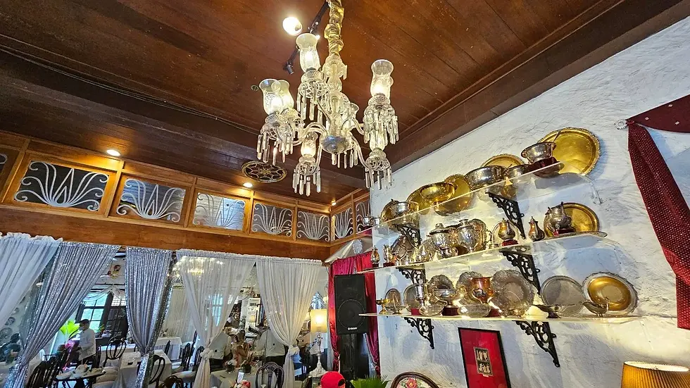 An ornate room featuring a crystal chandelier, decorative plates on shelves, and a richly decorated ceiling with framed glass panels.