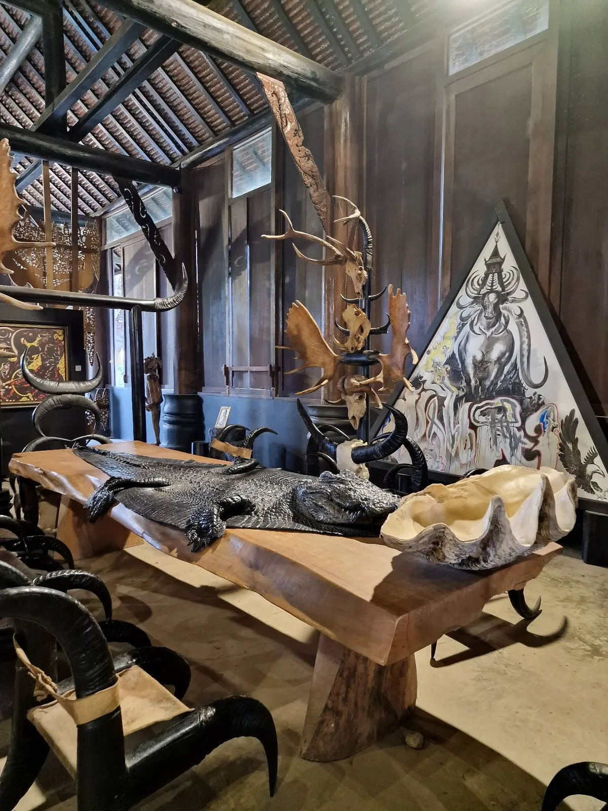 A room with rustic wooden furniture, a large wooden table, and decorative antlers on the wall. A triangular artwork is in the background.