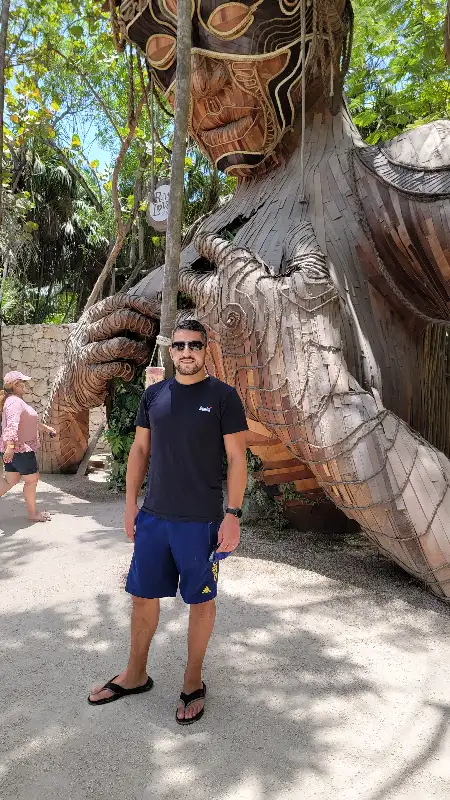 Leon standing in front of the massive Ven a la Luz wooden sculpture and other giant art installations at the Ahau Tulum Sculpture Park in Tulum, Riviera Maya, Mexico.